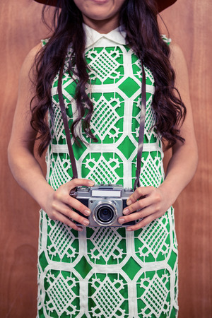 Mid section of woman holding camera against wooden wallの写真素材