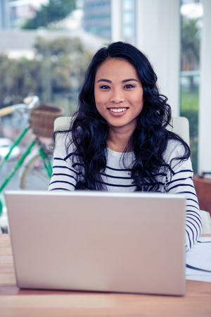 Smiling creative businesswoman using laptop in officeの写真素材