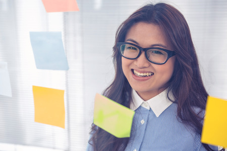 Asian businesswoman using sticky notes on wall in officeの写真素材