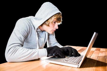 Focused man with hoodie typing on laptop with black backgroundの写真素材