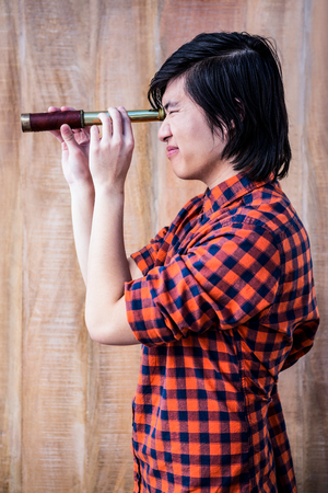 Hipster looking through a telescope on wooden backgroundの写真素材