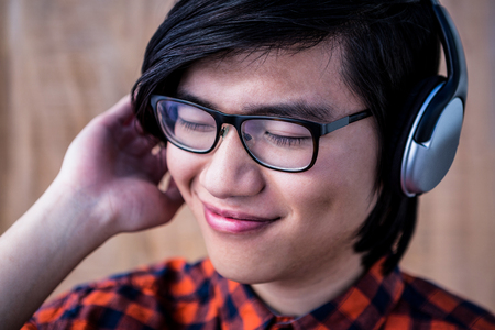Smiling hipster listening music with headphone on wooden backgroundの写真素材