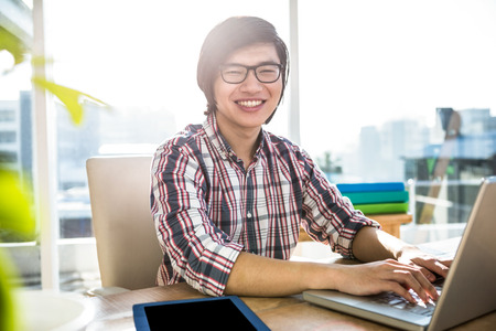 Smiling hipster businessman using laptop in officeの写真素材