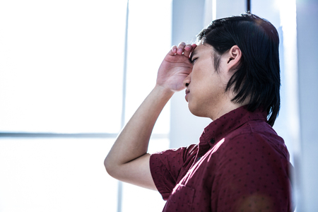 Worried creative businessman leaning on wall in officeの写真素材