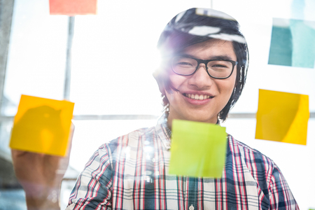 Creative businessman writing on sticky notes in officeの写真素材