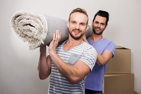 Gay couple carrying rolled up carpet at new homeの写真素材
