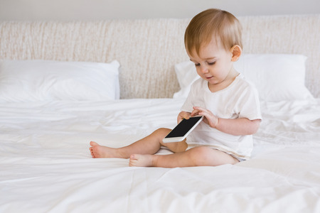 Cute baby using smartphone on bedの写真素材