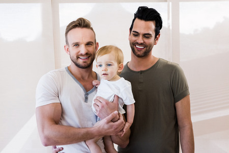 Smiling gay couple with child at homeの写真素材