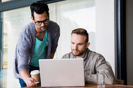 Focused gay couple using laptop outdoorsの写真素材