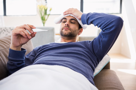 Sick man checking his temperature at home in the living roomの写真素材