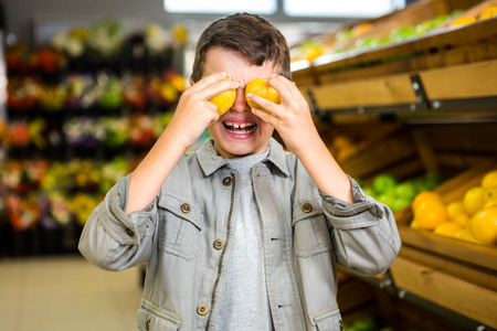 Cute boy covering his eyes with oranges at the grocery storeの写真素材