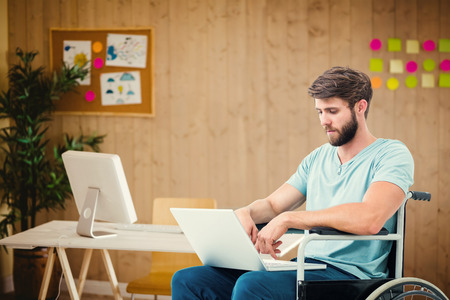 Man in wheelchair using computer against creative office with cool wooden panelingの写真素材