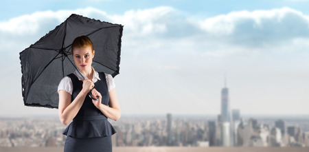 Pretty redhead businesswoman holding umbrella against balcony overlooking cityの写真素材