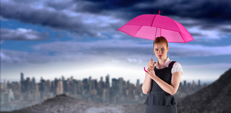 Pretty redhead businesswoman holding umbrella against large city on the horizonの写真素材