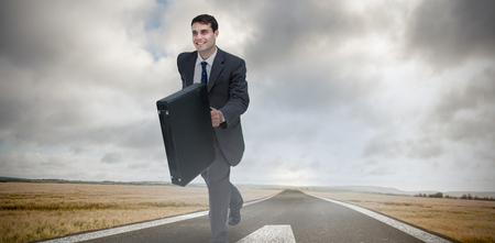 Smiling businessman in a hurry against green road landscapeの写真素材