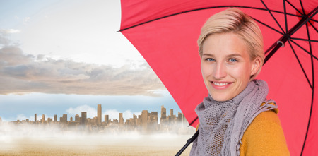 Smiling woman holding an umbrella against large city on the horizon past yellow fieldの写真素材
