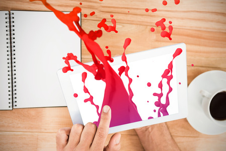 Pink paint splashes and drops against hands holding blank screen tabletの写真素材