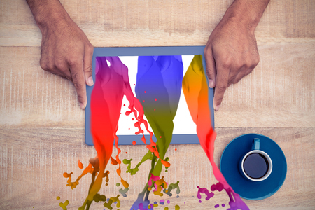 Pink paint splashes and drops against hand holding on digital tablet over table by coffeeの写真素材