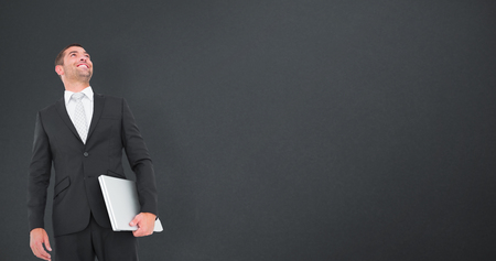 Businessman looking up holding laptop against grey backgroundの写真素材