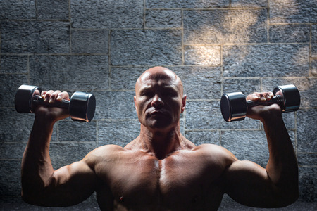 Portrait of man exercising with dumbbells against greyの写真素材
