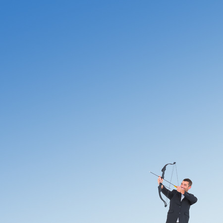 Businessman shooting a bow and arrow against blue skyの写真素材