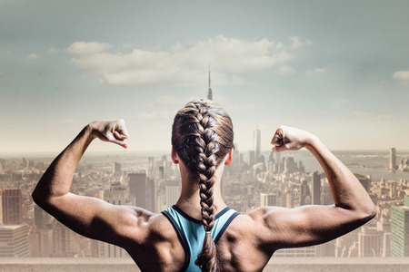 Rear view of woman with braided hair flexing muscles against balcony overlooking cityの写真素材
