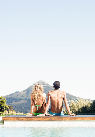 Rear view of couple sitting bu the pool looking at the landscapeの写真素材