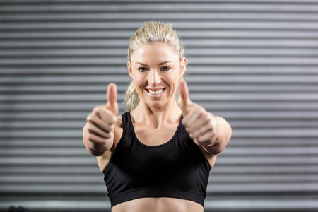 Fit woman showing thumbs up at crossfit gymの写真素材