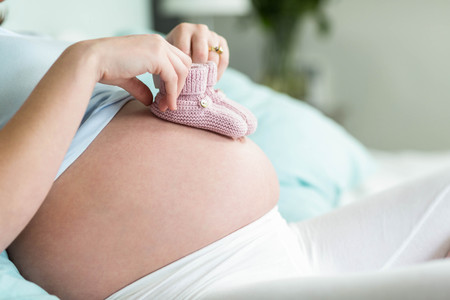 Pregnant woman with knitted slippers on her belly  in her bedroomの写真素材