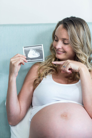 Pregnant woman showing an ultrasound picture lying on her bed