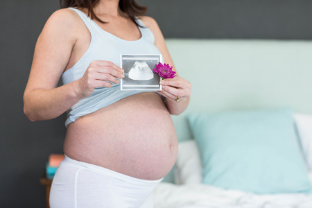 Pregnant woman holding an ultrasound scan in her bedroom