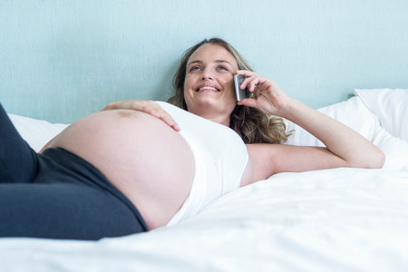 Pregnant woman making a phone call on her bedの写真素材