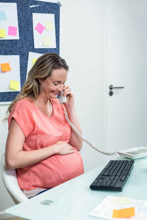 Pregnant woman using computer and phone in an officeの写真素材