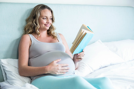 Pregnant woman reading a book lying on her bedの写真素材