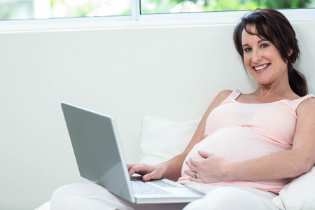 Pregnant woman relaxing with her laptop on bedの写真素材