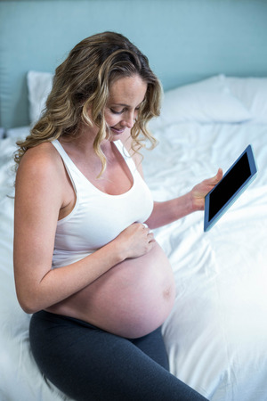 Pregnant woman using a tablet computer on her bedの写真素材