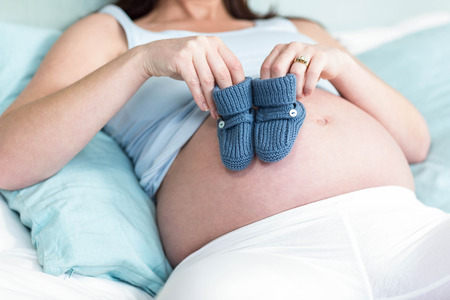 Pregnant woman with knitted slippers on her bellyin her bedroomの写真素材