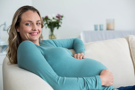 Pregnant woman touching her belly lying on the couchの写真素材