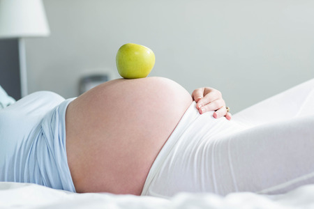 Pregnant woman with apple on belly at homeの写真素材