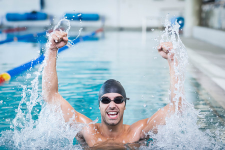 Handsome man triumphing with raised arms in the poolの写真素材