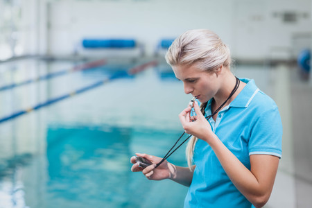 Pretty trainer looking at stopwatch at the poolの写真素材