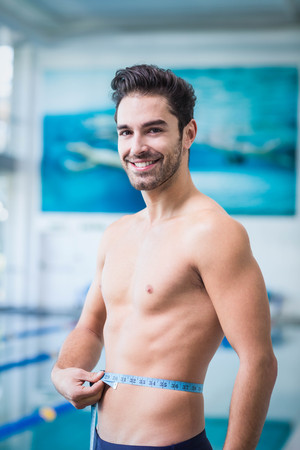 Handsome man measuring waist at the swimming pool