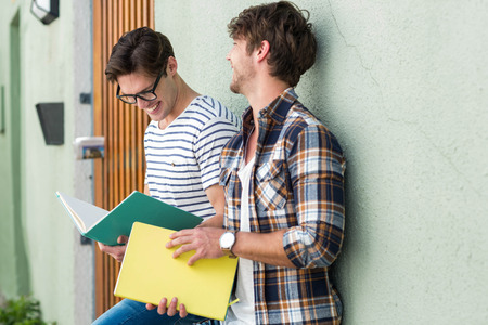 Hip men leaning against wall and holding notebooks on the streetの写真素材