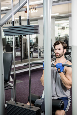 Focused man using weights machine for arms at the gym
