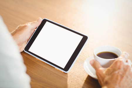Elderly man using tablet and drinking coffee at home