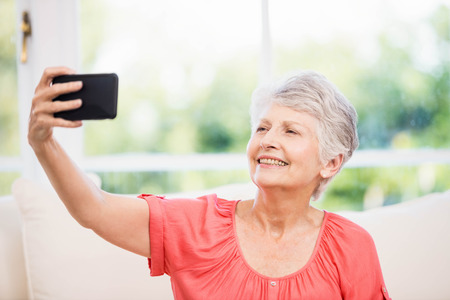 Happy senior woman taking selfie on the sofa