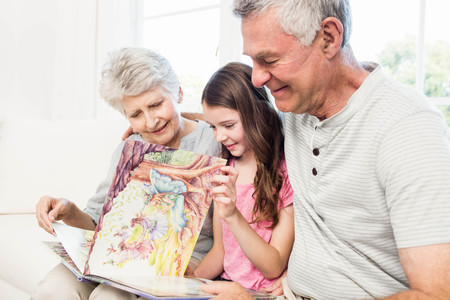 Happy grandparents with granddaughter reading a book on the sofaの写真素材