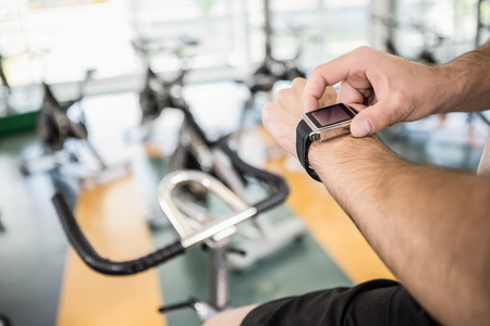 Close up of man using smartwatch on exercise bike at the gymの写真素材