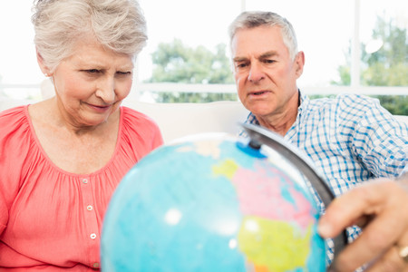 Smiling senior couple looking at globe on the sofaの写真素材