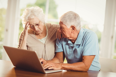 Worried senior couple using laptop at homeの写真素材